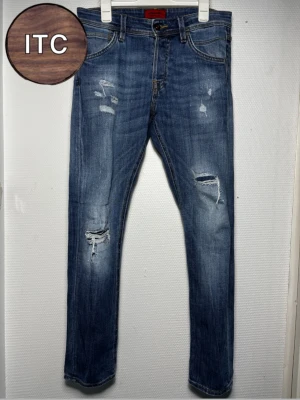 Jack & Jones jeans  - Säljer ett par blå slim jeans från Jack & Jones med snygga slitningar och trasiga detaljer på benen. Jeansen har klassisk femficksmodell, normal midja och är tillverkade i mjukt denimtyg. Perfekta för dig som gillar en avslappnad och trendig look.