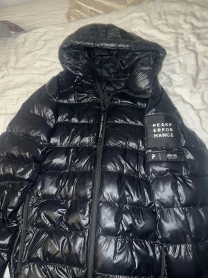 Svart pufferjacka Peak Performance - Säljer en svart pufferjacka från Peak Performance med huva och dragkedja. Storlek S men funkar även för M.Jackan har en quiltad design och en tydlig logga på armen. Perfekt för kalla dagar och riktigt skön att bära. Materialet är syntet och dun, vilket gör den både lätt och varm.
