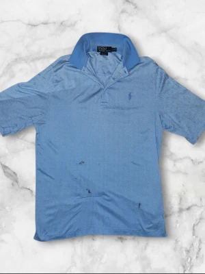 Blå mönstrad Polo Ralph Lauren skjorta - Säljer en blå kortärmad skjorta från Polo Ralph Lauren i modellen Golf Fit. Skjortan har ett diskret fiskbensmönster, klassisk krage och har den ikoniska broderade loggan på bröstet.