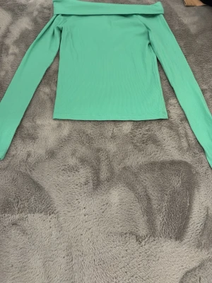 Grön offshoulder topp Kappahl - Snygg ribbad offshoulder topp från Kappahl i en fräsch grön färg. Toppen har långa ärmar och är tillverkad i ett mjukt, stretchigt material som sitter skönt på kroppen. Perfekt för dig som vill ha en enkel men trendig look. 