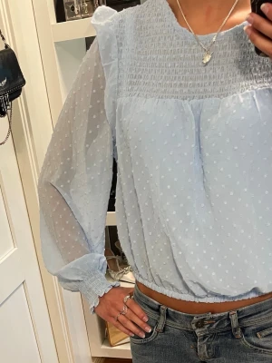 Ljusblå blus - Ljusblå blus med prickar och volanger. Passar XS/S. 