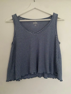 Blåvit randig linnetopp Hollister - Säljer en blå och vit randig linnetopp från Hollister. Toppen har v-ringning, är ärmlös och har en lös passform med vågig kant nertill. Perfekt för varma dagar och enkel att matcha med jeans eller shorts.