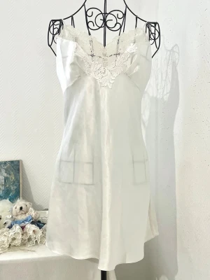 Vit bridal nattlinne från Victoria’s Secret - Elegant vit nattlinne i glansigt satin med tunna axelband och vacker spets längs v-ringad urringning både fram och bak. Storlek: S, passar 34 och 36. Dockan har storlek 34.