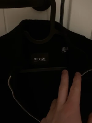Svart stickad overshirt från Only & Sons - Säljer en svart stickad overshirt från Only & Sons. Jackan har en clean look med hel dragkedja framtill och lång ärm. Perfekt för dig som gillar minimalistisk stil och vill ha något enkelt men snyggt att slänga på sig.