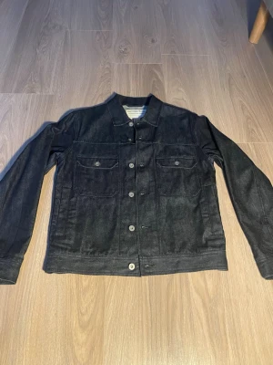  Universal Works jeansjacka XS - Säljer en  jeansjacka från Universal Works i storlek XS. Jackan har klassisk rak passform, två bröstfickor med knappar och stängs med silverfärgade knappar framtill. Tillverkad i 100% bomull för en skön och slitstark känsla.nypris typ 3900kr, mitt pris: 1249kr