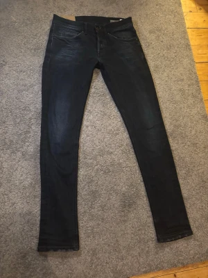Svarta skinny jeans från Dondup - Säljer ett par svarta skinny jeans från Dondup med klassisk femficksdesign och diskret slitning på låren. Jeansen har låg midja och smal passform hela vägen ner. Materialet är stretchigt jeans för extra komfort och rörelsefrihet. 