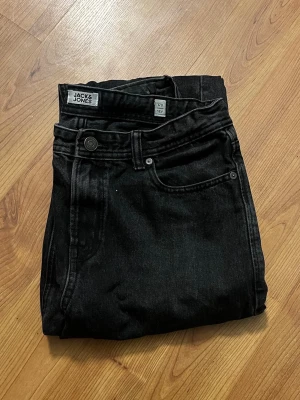 Svarta jeans från Jack & Jones - Säljer ett par svarta jeans från Jack & Jones i klassisk femficksmodell. Jeansen har raka ben och normal passform, tillverkade i slitstarkt bomullsmaterial. Snygg tvättad svart färg och enkla detaljer gör dem perfekta till alla outfits.