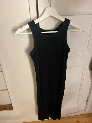 Svart ribbad linneklänning från 157 - Säljer en svart ribbad linneklänning från 157 i storlek XS. Den är ärmlös med breda axelband och har en tight passform. Tillverkad i 100% bomull vilket gör den mjuk och skön att bära. Perfekt till sommaren och enkel att matcha med olika stilar.
