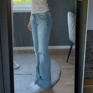 Ljusblå bootcut jeans med slitningar - Säljer ett par ljusblå jeans med bootcut passform och snygga slitningar vid knäna. Jeansen har låg midja och klassisk femficksdesign. Perfekta för dig som gillar en avslappnad och trendig look. Materialet är mjukt denim i bomull. Originalpris är 699kr. Hittade tyvärr inga bra bilder på dom. Pris kan diskuteras. Midjemått 31-32cm och innerbenslängd är ca 82cm. Är lite slitna längst ner vid fötterna men knappt