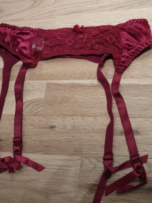Vinröd strumpebandshållare  - Säljer en vinröd strumpebandshållare från Adelsten med spetsdetaljer och glansigt satin material. Den har justerbara band och små rosetter framtill. Stängs med hyskor bak och har en elegant, feminin look. Perfekt för alla hjärtans dag  / Valentine's day. Jag har fler annonser uppe och ger mängd rabatt, så kolla gärna min sida!