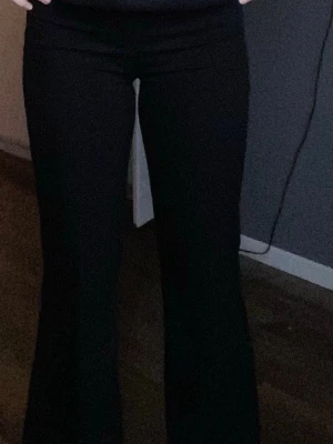 Flare kostymbyxor från Design by Si - Säljer ett par svarta bootcut byxor med snygga fickdetaljer bak. Byxorna har knapp och dragkedja framtill samt bälteshällor. Materialet är stretchigt och sitter tajt upptill men släpper ut vid benen för en clean siluett.