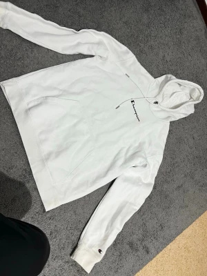 Champion vit tröja  - Vit Champion hoodie i storlek L. Klassisk modell med huva och magficka. Broderad Champion-logga på bröstet samt dekorativa loggor längs ärmarna. Mjuk och bekväm kvalitet, i gott skick.
