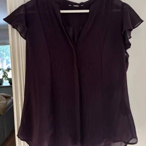 Mörklila - Säljer en mörklila blus. Blusen har en lätt transparent känsla och en lös passform, perfekt för dig som gillar stilrena och eleganta plagg. Ingen synlig logga eller märke.