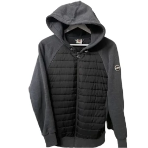 Svart och mörkgrå hoodie från Colmar - Snygg hoodie från Colmar i svart och mörkgrått med quiltad frontpanel och dragkedja. Tröjan har huva, långa ärmar och en logga på ärmen. Perfekt för kyliga dagar och streetstyle.