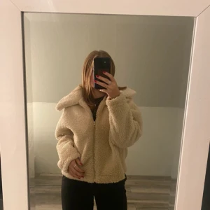 Beige teddyjacka från Gina Tricot - Supermjuk och fluffig teddyjacka från Gina Tricot i beige färg. Jackan har dragkedja framtill, stor krage och en loose passform. Perfekt för kyliga dagar när du vill vara både varm och snygg.