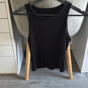 Svart ribbad linnetopp - Säljer en svart ribbad linnetopp med rund halsringning. Toppen är ärmlös och har en enkel, stilren design som passar perfekt till jeans eller kjol. Materialet känns mjukt och följsamt mot kroppen.