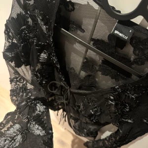Svart blommig meshblus Gina Tricot - Säljer en svart transparent meshblus från Gina Tricot med broderade blommor och snygg snörning framtill. Oanvänd! 