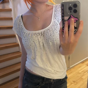 Vit blus med paljetter från H&M - Säljer en vit blus från H&M med glittriga paljettdetaljer över bröstet och axlarna. Blusen har en rundad, vid urringning och korta ärmar. 