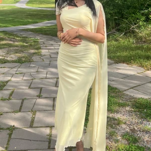 Ljusgul långklänning med släp - Elegant ljusgul långklänning i ett mjukt, följsamt material. Klänningen har oneshoulder-design och ett långt, svepande släp som ger en extra dramatisk look. Figurnära passform som framhäver siluetten. Perfekt för dig som vill sticka ut med en stilren och modern look. Själv har jag bärt den endast en gång på en möhippa fest! 