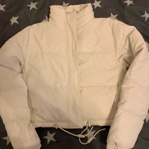 Vit pufferjacka från FB Sister, M - Snygg vit pufferjacka från FB Sister i storlek M Jackan har hög krage, dragsko i midjan och långa ärmar. Tillverkad i syntetmaterial med quiltade partier för extra värme. Perfekt för kalla dagar när du vill hålla stilen enkel och clean.