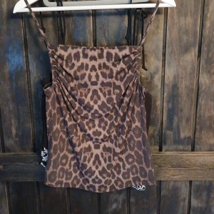Leopardmönstrad linnetopp H&M XS - Säljer en brun leopardmönstrad linnetopp från H&M i storlek XS. Toppen har tunna axelband och rynkade detaljer framtill som ger en snygg draperad effekt. Perfekt att styla med jeans eller kjol för en trendig look.