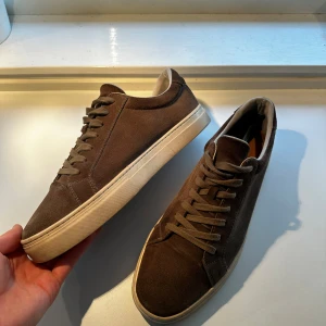 Bruna mockasneakers från Vagabond - Snygga bruna sneakers från Vagabond i mocka med beige sula och klassisk snörning. Skorna har en stilren och minimalistisk design med rund tå och platt sula, perfekta till jeans eller chinos. Fodrade med ljus insida för extra komfort.