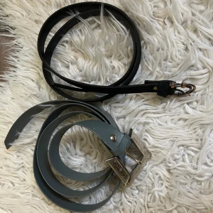 Två skärp  - Säljer två snygga bälten: ett svart smalt bälte med kopparfärgat spänne och ett ljusblått bälte med ett fyrkantig silverspänne. Perfekta accessoarer för att lyfta din outfit med coola detaljer och stilrena färger.