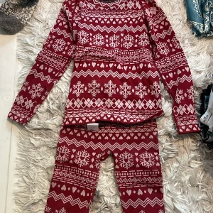Röd julset - Röd långärmad tröja med vitt julmönster och byxorna till, snöflingor och hjärtan. Perfekt för vinterns mysiga dagar. Tröjan har klassiskt rund halsringning och är i mjukt material.