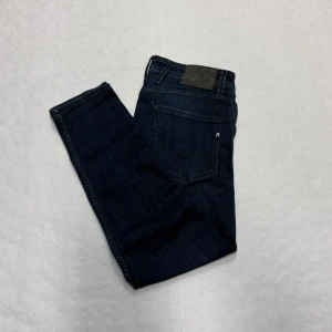 Mörkblå Replay Anbass - Säljer ett par mörkblå jeans från Replay med klassisk femficksdesign och raka ben. Jeansen har subtila slitningar framtill och en snygg tvätt som ger en cool look. Materialet är mjukt jeans och passformen är normal med medelhög midja.