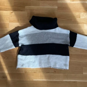 Randig polotröja från SHEIN XS - Säljer en stickad polotröja från SHEIN i storlek XS. Tröjan har breda ränder i svart, grått och vitt, hög polokrage och lång ärm. Perfekt för kyliga dagar och ger en chill vibe till din outfit.