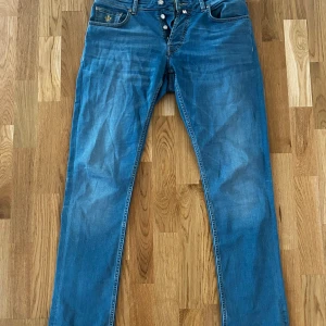 Blå jeans Steve Satin från Morris - Snygga blå jeans från Morris, modell Steve Satin. Klassisk femficksdesign med raka ben och gul kontrastsöm. Tillverkade i bomull med en liten del elastan för extra komfort. Perfekta för dig som gillar en stilren och tidlös look.