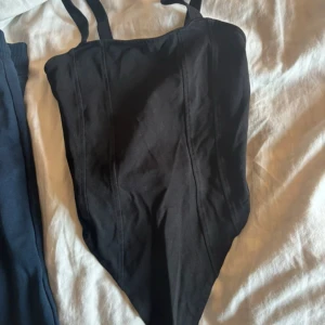 Svart korsett-body från H&M XS - Aldrig använd. Svart korsett-topp från H&M i storlek XS. Toppen har smala axelband och markerade sömmar framtill som ger en snygg form. Den är sydd i ett stretchigt bomullsmaterial och har en spetsig nederkant framtill för en trendig look. 