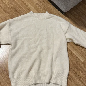 Vit stickad tröja med ribbade muddar - Mysig vit stickad tröja med ribbad hals, ärmslut och nederkant. Enkel och stilren design som passar perfekt till lager-på-lager. Tröjan har lång ärm och en något lös passform för extra komfort.