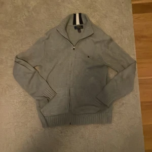 Grå kofta från Polo Ralph Lauren - Snygg grå kofta från Polo Ralph Lauren med dragkedja framtill och ribbade muddar. Tröjan har hög krage med vit och marinblå randig detalj på insidan. Perfekt för lager-på-lager och chill stil.