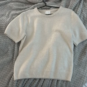 Beige stickad kortärmad tröja H&M - Supermjuk och stilren beige stickad tröja från H&M med korta ärmar och rund hals. Perfekt för lager-på-lager och funkar året runt. Ribbstickade muddar vid ärmslut och nederkant ger en clean look.