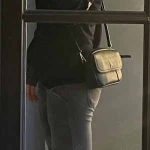 Svart axelväska i skinn med dragkedja - Säljer en stilren svart axelväska i skinn med justerbar rem och guldfärgade metalldetaljer. Väskan har en praktisk dragkedja upptill och ett extra fack framtill med lock. Perfekt storlek för mobil, plånbok och andra småsaker. Även köpt i Italien men säljer pågrund av behöver lagas på båda sidorna(se sista bild)🙃