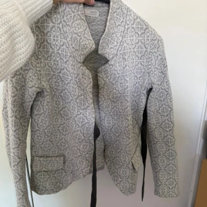 Grå mönstrad cardigan jacka - Snygg grå cardigan jacka från Odd Molly med ljusgrått geometriskt mönster. Jackan har två fickor framtill, lång ärm och en öppen design utan knäppning. Perfekt för lager-på-lager och chill vardagsstil.