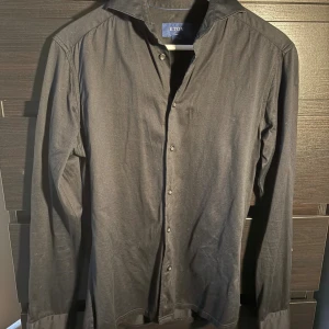 Svart skjorta från Eton slim fit - Svart skjorta från Eton i slim fit med klassisk krage och knappar framtill. Skjortan är långärmad och tillverkad i mjuk bomull som känns skön mot huden. Perfekt för dig som gillar stilrena och enkla plagg med snygg passform.