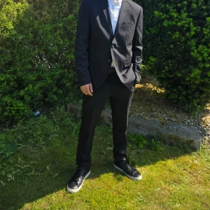 Svart kostym med kavaj  - Säljer en klassisk svart kavaj. Kavajen har två knappar, fickor med lock och en stilren passform. Perfekt till student eller bal. Kostymen är helsvart och har en snygg, tidlös look.Jack & Jones.JPRFRANCO SUIT NOOS.Använd bara 1 gång  