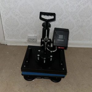  värmepress för textiltryck - Digital värmepress med justerbar temperatur och timer, perfekt för textiltryck på t-shirts och andra plagg. Utrustad med digital display och robust handtag. Maskinen ser ut att vara i mycket gott skick utan synligt slitage eller defekter.