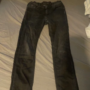 Svarta jeans från Tommy Hilfiger - Säljer ett par svarta jeans från Tommy Hilfiger i storlek 164. Jeansen har klassisk femficksdesign, raka ben och snygga detaljer med röda sömmar vid linningen. Materialet är jeans och färgen är mörksvart, perfekt för en stilren look.
