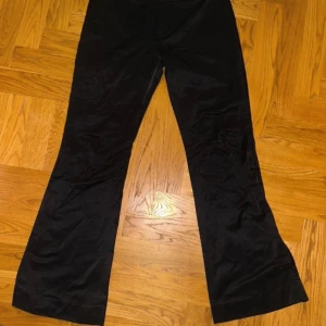 Svarta vida byxor i satin-look - Snygga svarta byxor med glansig satin-look och vida ben. Byxorna har en klassisk passform med låg midja och är perfekta för dig som gillar en trendig och stilren vibe. Materialet känns mjukt och följsamt mot huden.