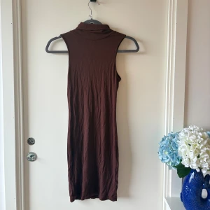 Brun ribbad ärmlös klänning - Säljer en brun, ärmlös klänning med polokrage och ribbad struktur. Klänningen är kroppsnära och har en enkel, stilren design som passar perfekt för dig som gillar minimalistiskt mode. Materialet känns mjukt och stretchigt.