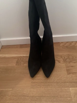 Svarta höga mockastövlar med klack - Snygga svarta stövlar i mocka med spetsig tå och bred klack. Stövlarna är knähöga och har en stilren design som passar perfekt till höstens och vinterns outfits.