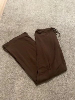 Bruna mjukisbyxor från nelly - Mysiga bruna mjukisbyxor med dragsko i midjan. Byxorna har en loose passform och raka ben, perfekta för chill dagar hemma eller när du vill vara extra bekväm. Tillverkade i mjukt material som känns skönt mot huden. Från nelly och inga skadar förutom att de är lite nopprigt mellan låren. Köpt för 349kr.