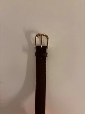 Brunt läderbälte med silverfärgat spänne - Brunt bälte i läder med ett guldfärgat spänne. Passar till både jeans och kostymbyxor. 