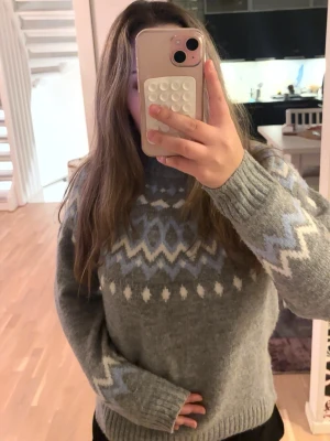 Grå stickad tröja med mönster - Mysig grå stickad tröja med vitt och ljusblått nordiskt mönster runt halsen och ärmarna. Tröjan har ribbade muddar vid ärmslut och nederkant, samt en avslappnad passform. Perfekt för kalla dagar och enkel att matcha med jeans. Perfekt nu under vintern💕