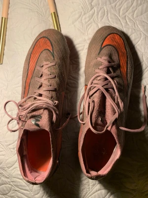 Nike Mercurial rosa fotbollsskor - Säljer ett par Nike Mercurial fotbollsskor i rosa med orange och svarta detaljer. Skorna är i ett använd skick och säljs därför väldigt billigt.