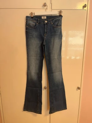 Bootcut jeans  - Snygga blå bootcut jeans från ONLY med klassisk femficksdesign och knappgylf. Jeansen har en lätt utsvängd passform nedtill och är tillverkade i mjukt denimtyg som ger en bekväm känsla. Perfekta för dig som vill ha en tidlös och trendig look.
