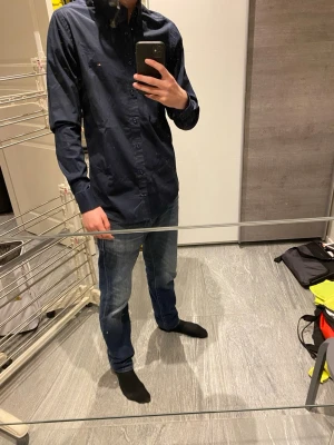 Mörkblå skjorta Tommy Hilfiger S - Säljer en mörkblå skjorta från Tommy Hilfiger i slim fit stretch. Skjortan har klassisk krage, knappar hela vägen och den ikoniska lilla loggan på bröstet. Perfekt till jeans eller chinos för en clean look.